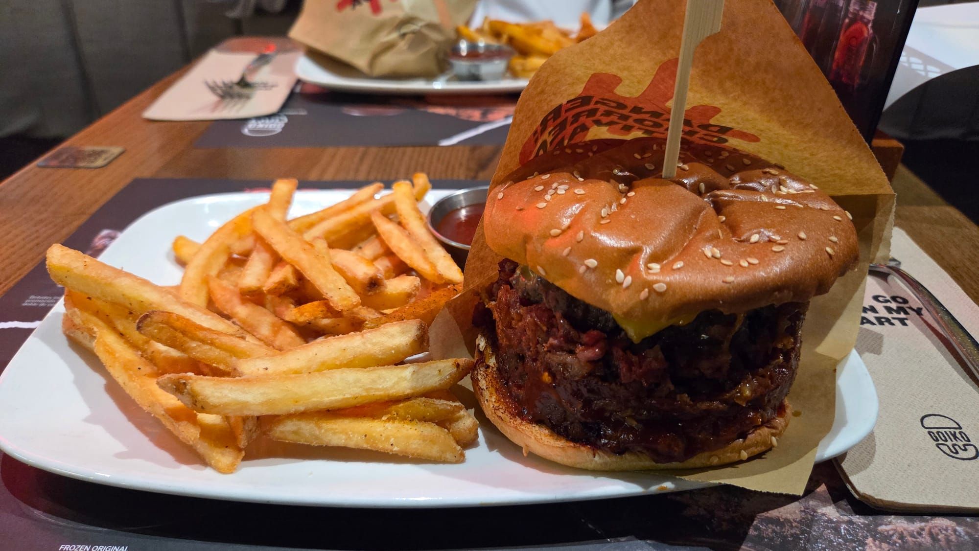 A burger with a sesame bun beside a pile of fries on a white plate.