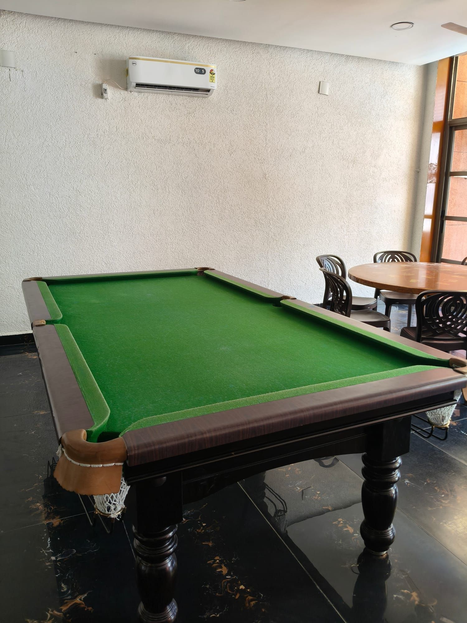 A pool table with green felt in a bright room, with a few cafe tables behind it.
