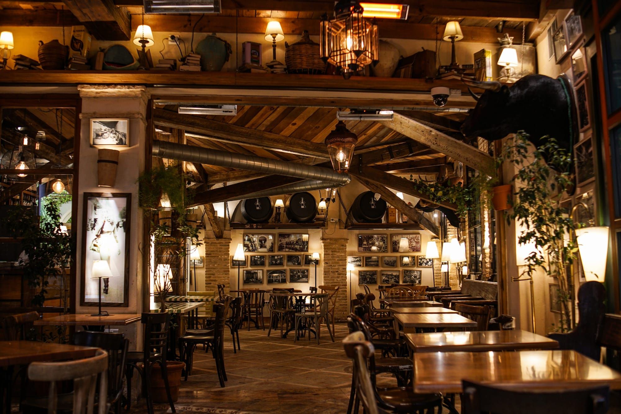 A long wood-beamed room with lantern lights, framed pictures on the walls and dark wood tables.